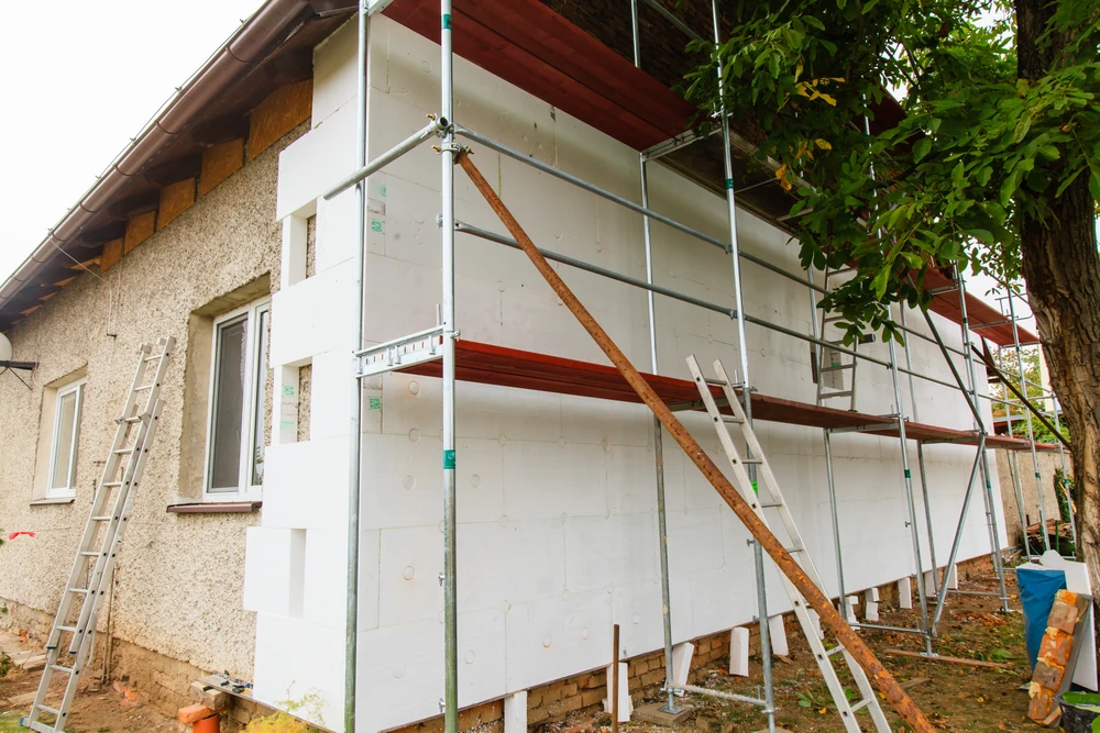 Ouvrier en bâtiment installant un panneau d'isolation thermique extérieure sur façade de maison en construction