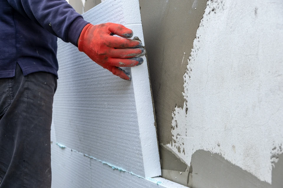 Ouvrier en bâtiment installant un panneau d'isolation thermique extérieure sur façade de maison en construction